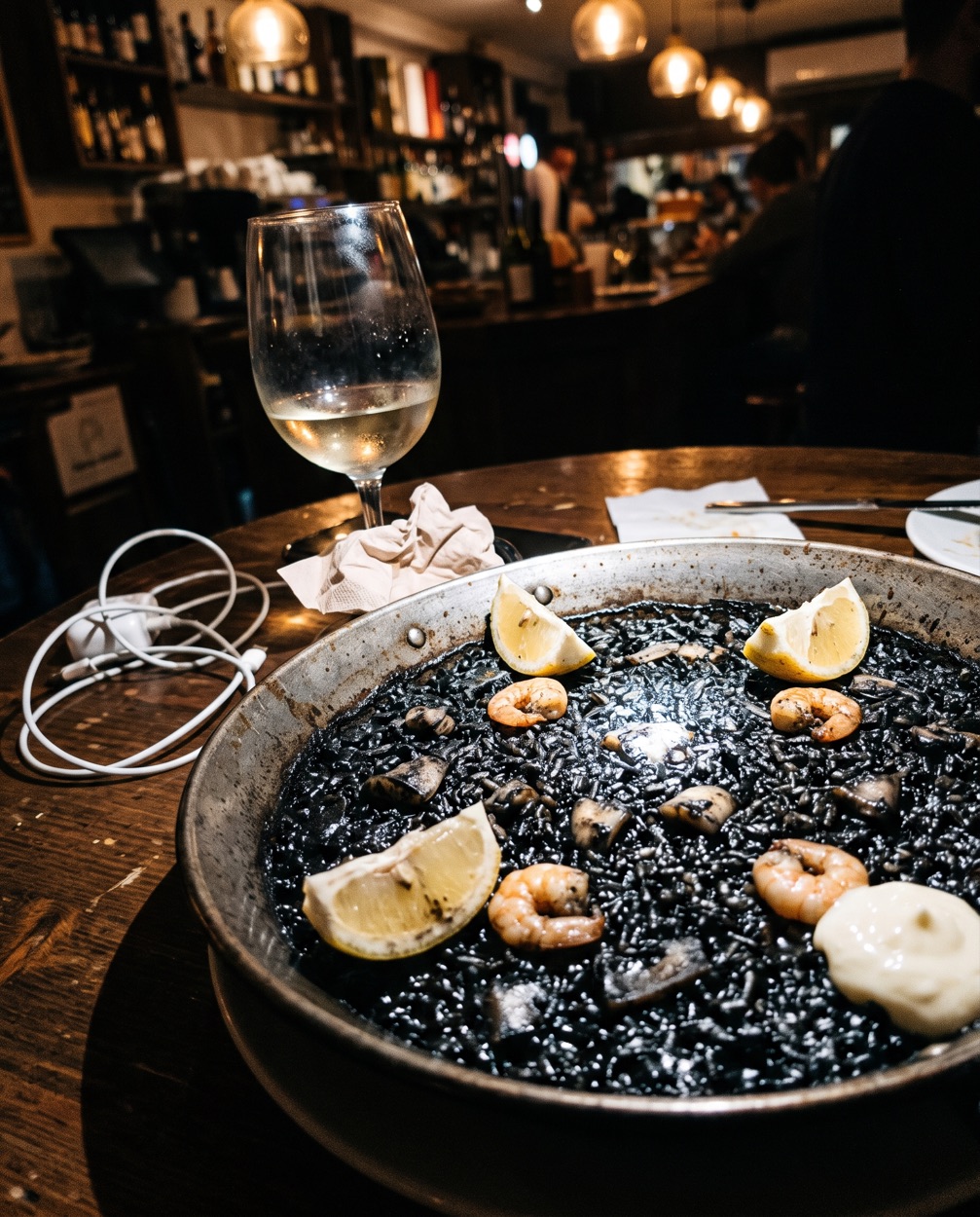 Antes: arròs negre fotografiado con el móvil y flash en una mesa con servilletas y un cargador